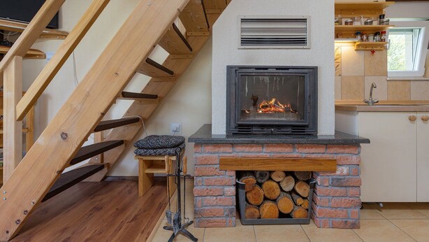A modern kitchen with a fireplace, wooden staircase, and a small seating area. - House Jasenak (Gracac)