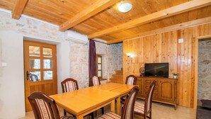 Une table à manger en bois, accompagnée de six chaises, un téléviseur posé sur un meuble en bois et des murs en pierre.