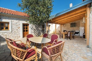 A stone building with a tiled roof, a wooden pergola, wicker furniture, and a stone table. - House Stone Curlew 1 (Benkovac)