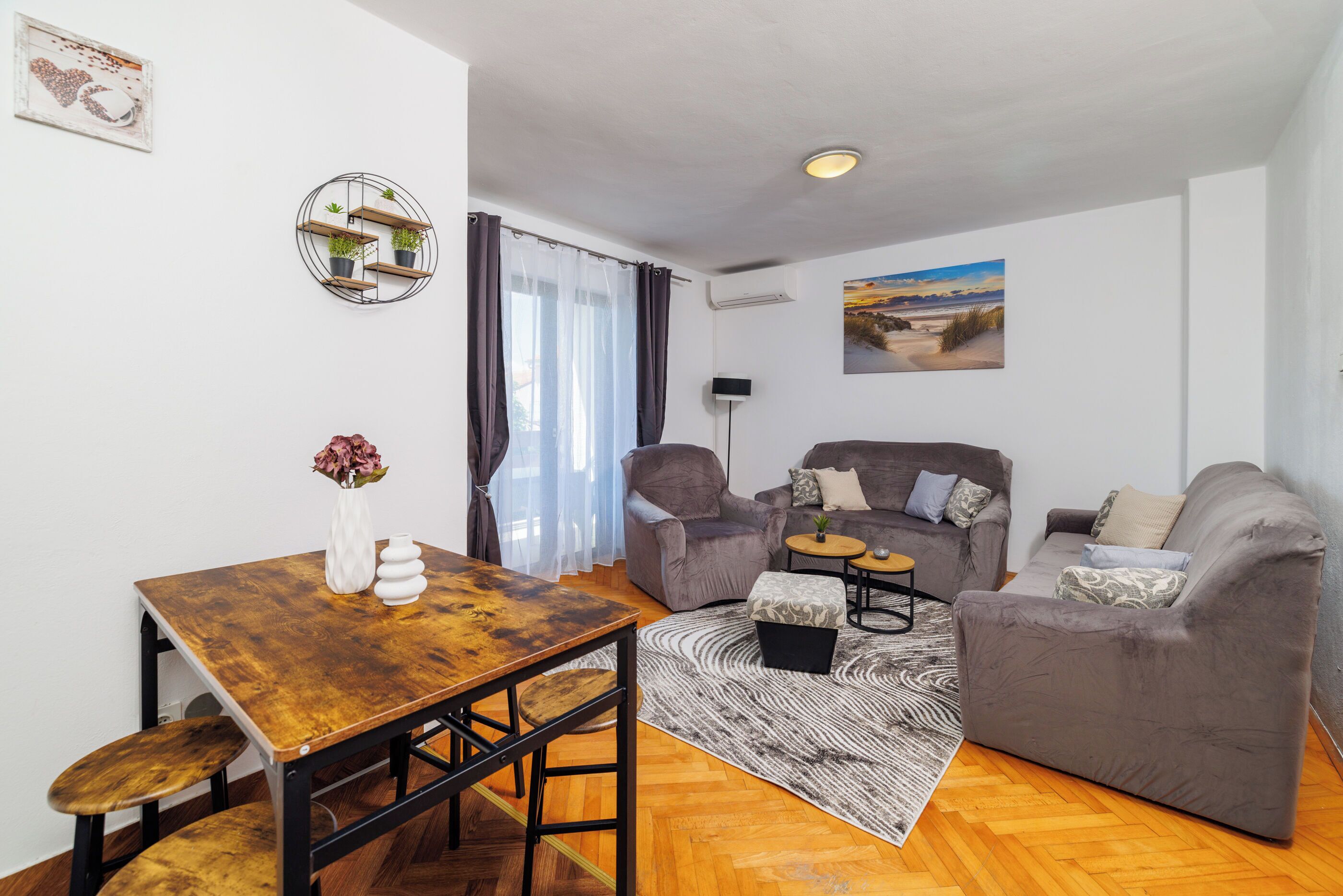 A living room with a wooden table, two grey sofas, a small round coffee table, and a patterned rug.