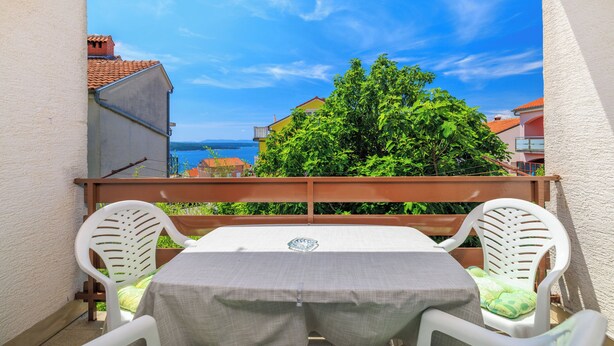 Ein Balkon mit Tisch und zwei Stühlen, der auf ein Gewässer und Gebäude blickt.