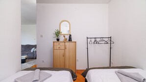 Ein Zimmer mit zwei Betten, einem Holzschrank, einem Spiegel, einer Pflanze und einem Kleiderständer.
