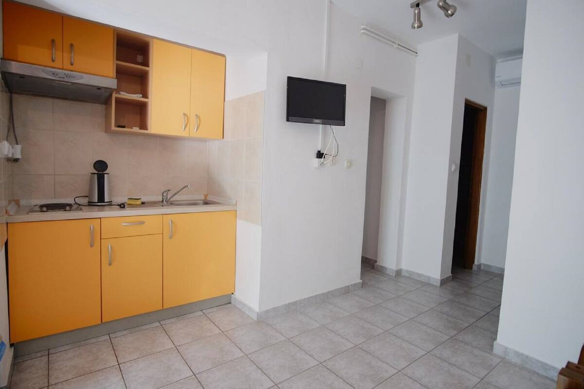 A kitchen with yellow cabinets, a sink, and a flat-screen TV mounted on the wall.