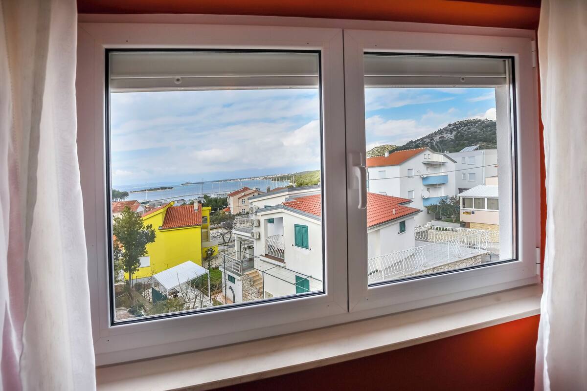 A window with a view of a coastal town, including buildings and a body of water.