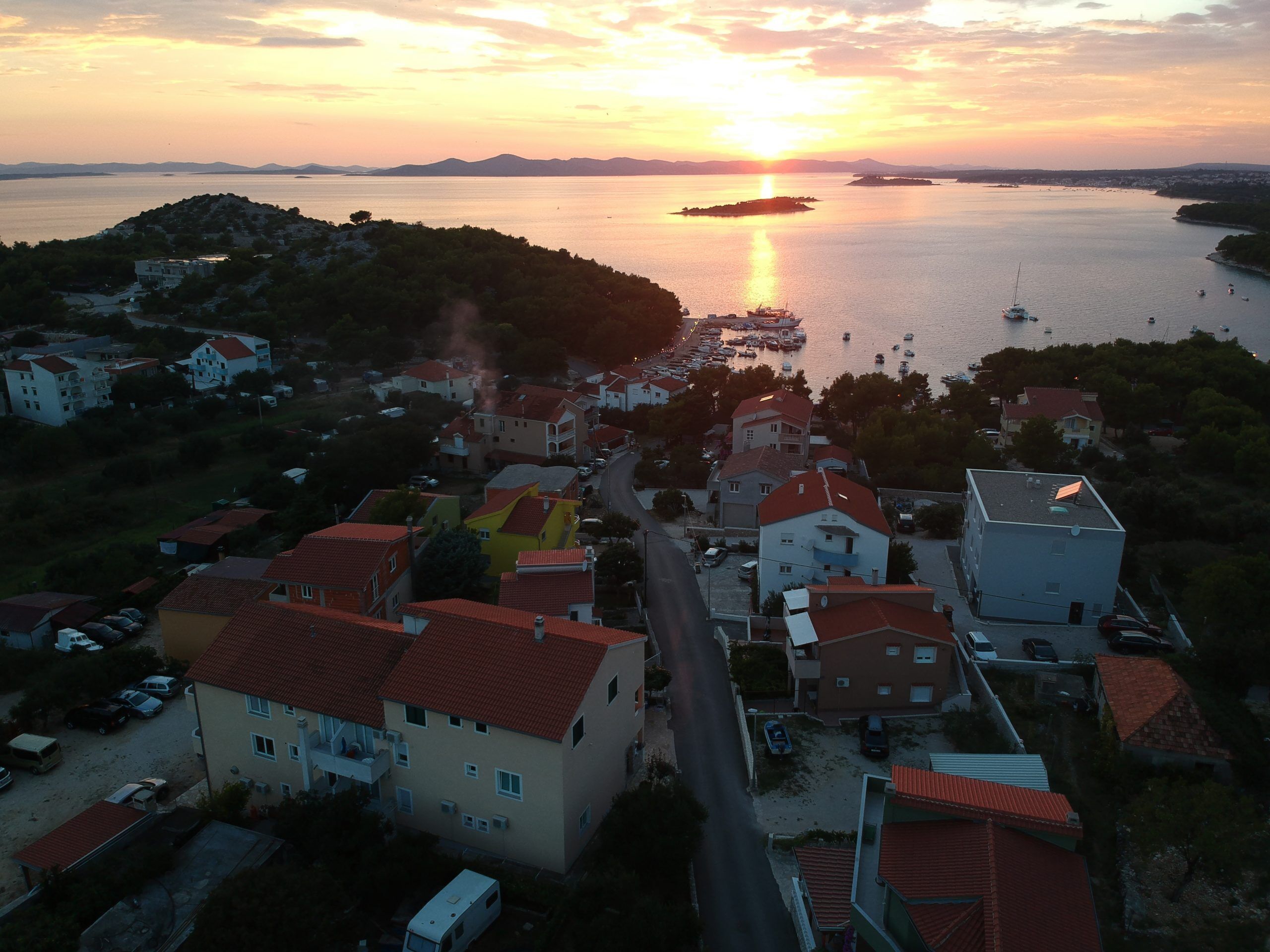 A coastal town with buildings along the waterfront, a clear view of the sea, and a sunset in the background.
