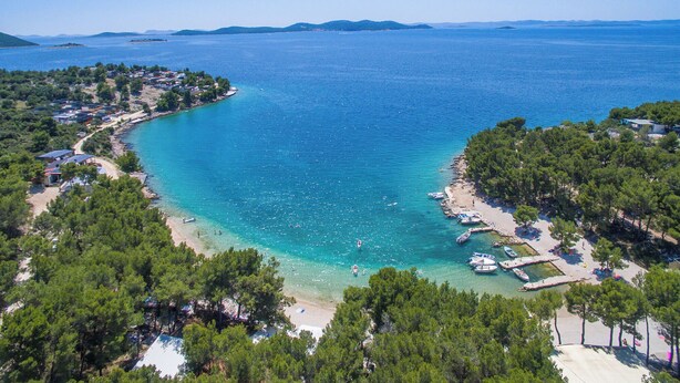 An aerial view of a coastal area with a beach, boats, and buildings. - Apartments Rucmarin (Pakostane)
