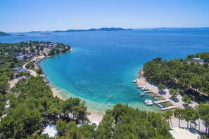 An aerial view of a coastal area with a beach, boats, and buildings. - Apartments Rucmarin (Pakostane)
