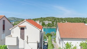 A coastal building with a red-tiled roof, a visible staircase, and a view of a turquoise sea and green hills in the background. - Apartment Niko (Sibenik)