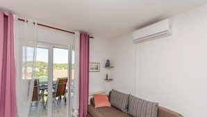 A living room with a sofa, a table with chairs, and a view of greenery outside. - Apartment Niko (Sibenik)