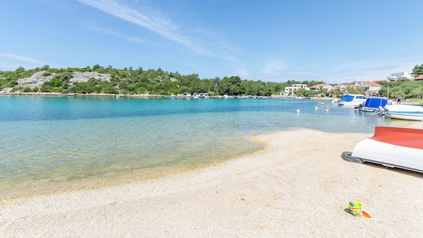 A beach with clear water, boats, and a rocky hill in the background. - Apartment Niko (Sibenik)
