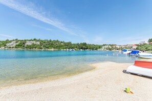 Una spiaggia con acque cristalline, imbarcazioni e una collinetta rocciosa sullo sfondo.