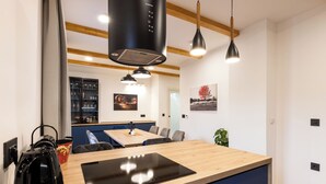 A modern kitchen with a wooden countertop, black kettle, and built-in stove. There is a dining area with chairs and a table, and a plant on the right. - House Medvjed (Ravna Gora)