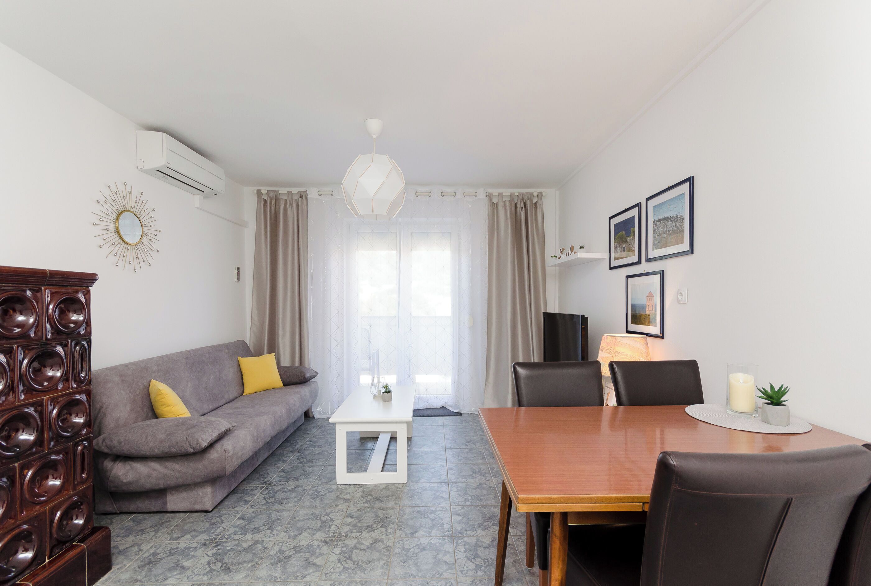 A modern living room with a grey sofa, a wooden dining table, and a white coffee table.