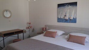 Et hotelværelse med en seng, et skrivebord, en lampe og et maleri af sejlbåde.