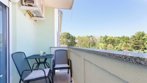 En balkon med to stole og et bord, en lille potteplante og udsigt til træer og bygninger.
