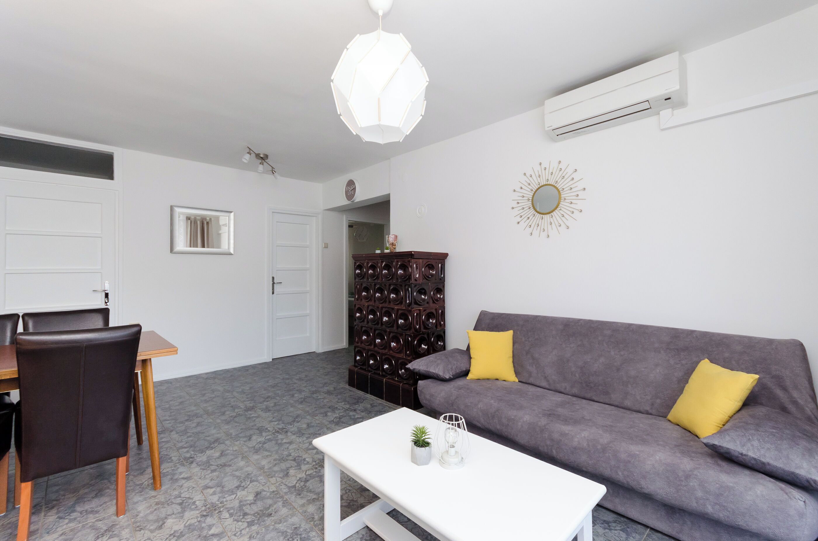 A modern living room with a grey sofa, wooden dining table, and chairs.