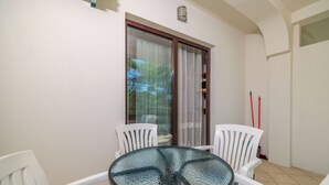 Een klein balkon met een glazen tafel, witte stoelen, een schuifpui en een rode bezem die tegen de muur staat.