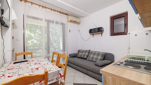 Een knus woongedeelte met een eettafel, stoelen, een bank, een klein keukentje met een spoelbak en een airconditioning.