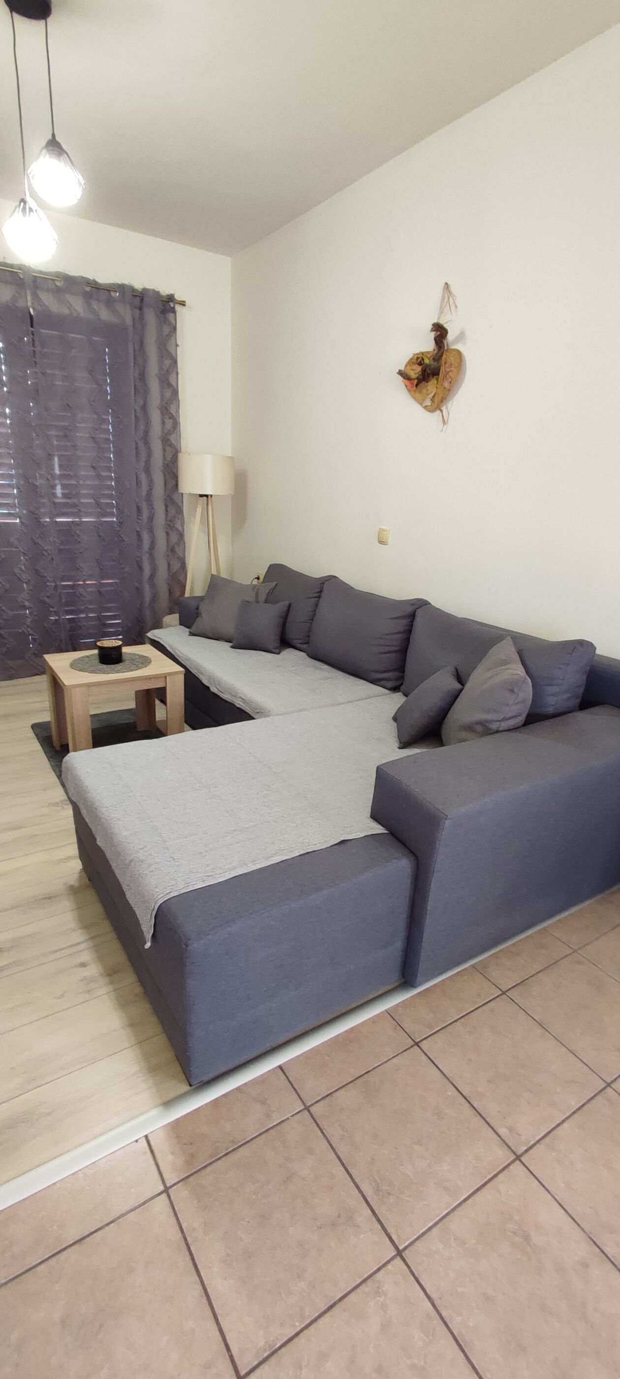 A modern living room with a grey sectional sofa, a small wooden side table, and a decorative wall piece.