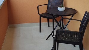 Ein kleiner Sitzbereich im Freien mit zwei Stühlen und einem Tisch, einem gefliesten Boden und einer schlichten, orangefarbenen Wand.