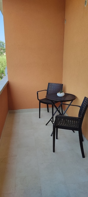 Ein kleiner Sitzbereich im Freien mit zwei Stühlen und einem Tisch, einem gefliesten Boden und einer schlichten, orangefarbenen Wand.
