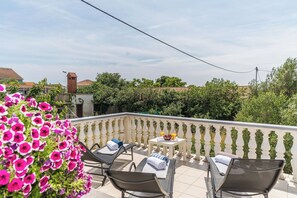 Un balcón con dos sillones de relax, una mesita con una bandeja de fruta y vistas a una zona residencial con árboles y casas.