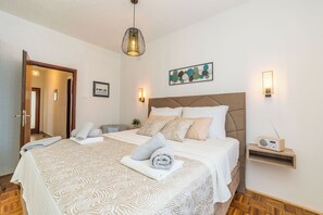 A hotel room with a large bed, a bedside table, a wall-mounted radio, and a door leading to another room. - Apartment Felix (Sukosan)