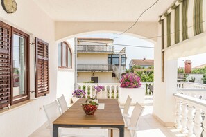 A balcony with a wooden table and chairs, a potted plant, and a view of neighboring buildings. - Apartment Felix (Sukosan)
