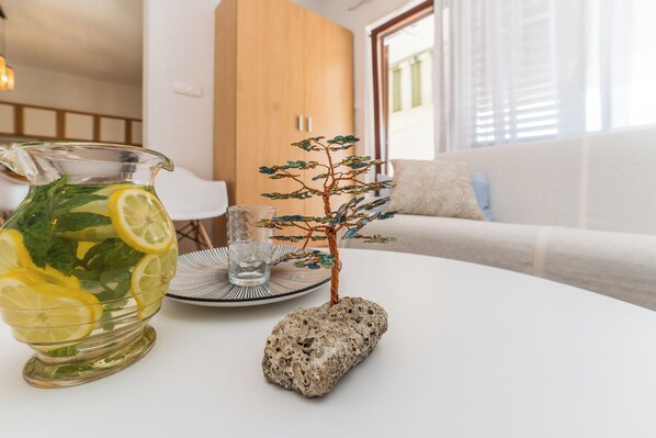 A clear glass pitcher with lemon slices and mint leaves on a white table, a small tree sculpture, and a rock. - Apartment Felix (Sukosan)