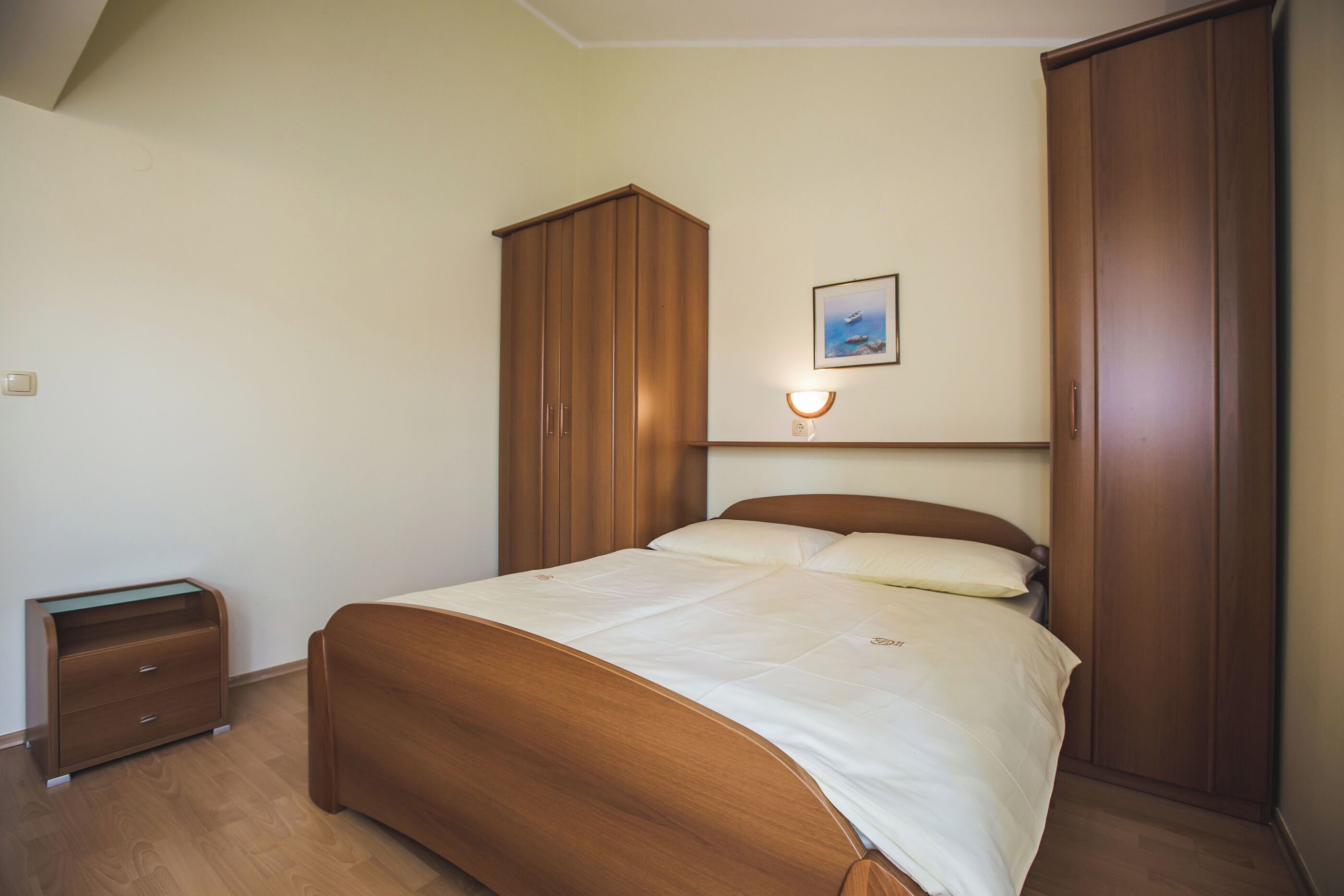 A bedroom with a wooden bed, a nightstand, a wardrobe, and a wall-mounted light fixture.