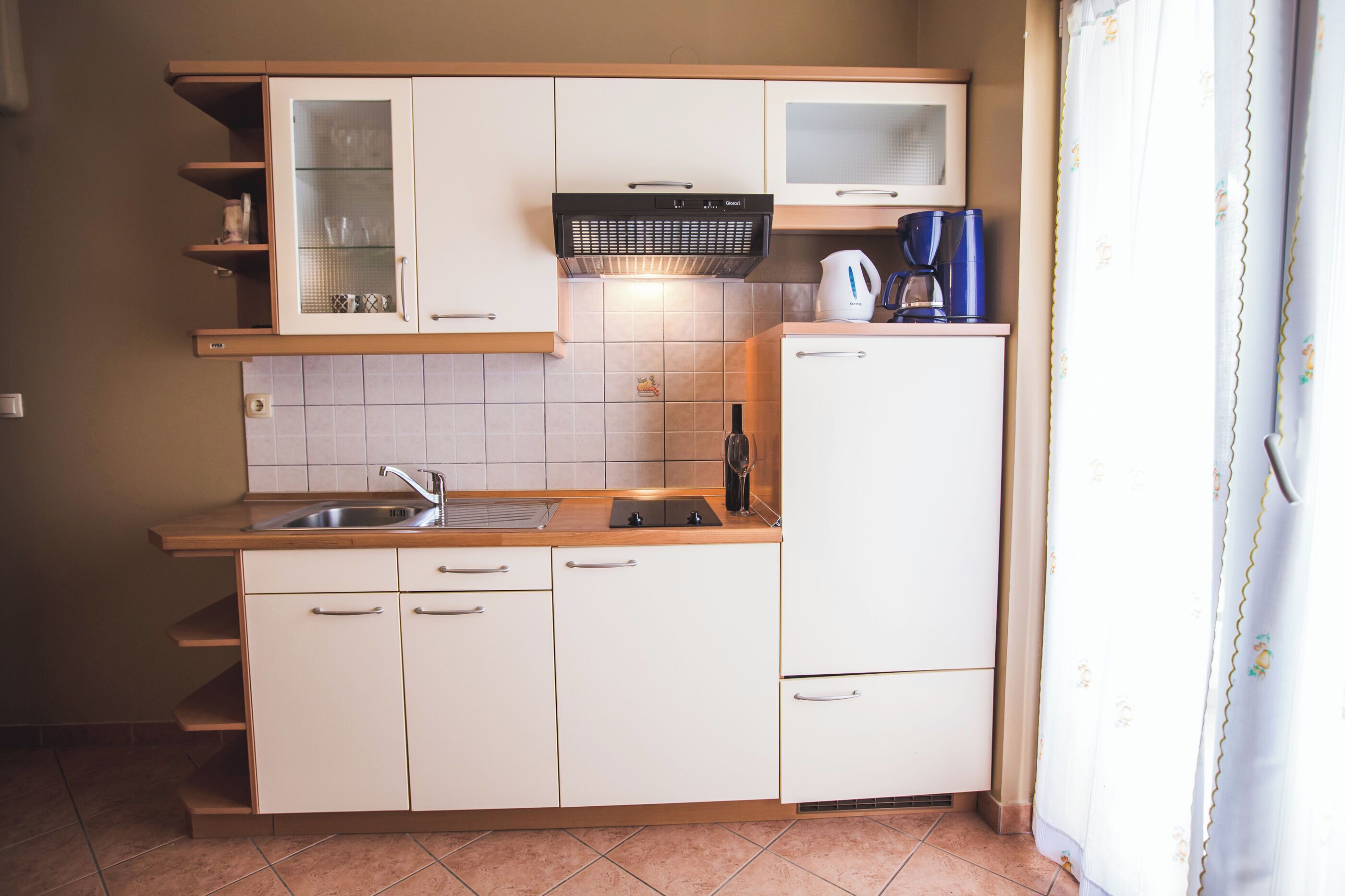 A compact kitchen with white cabinets, a built-in oven, a coffee maker, and a sink.