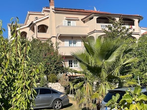 A multi-story building with a beige facade and red-tiled roof. There are balconies with railings and windows with shutters. - Apartments Anamarija S (Lopar)