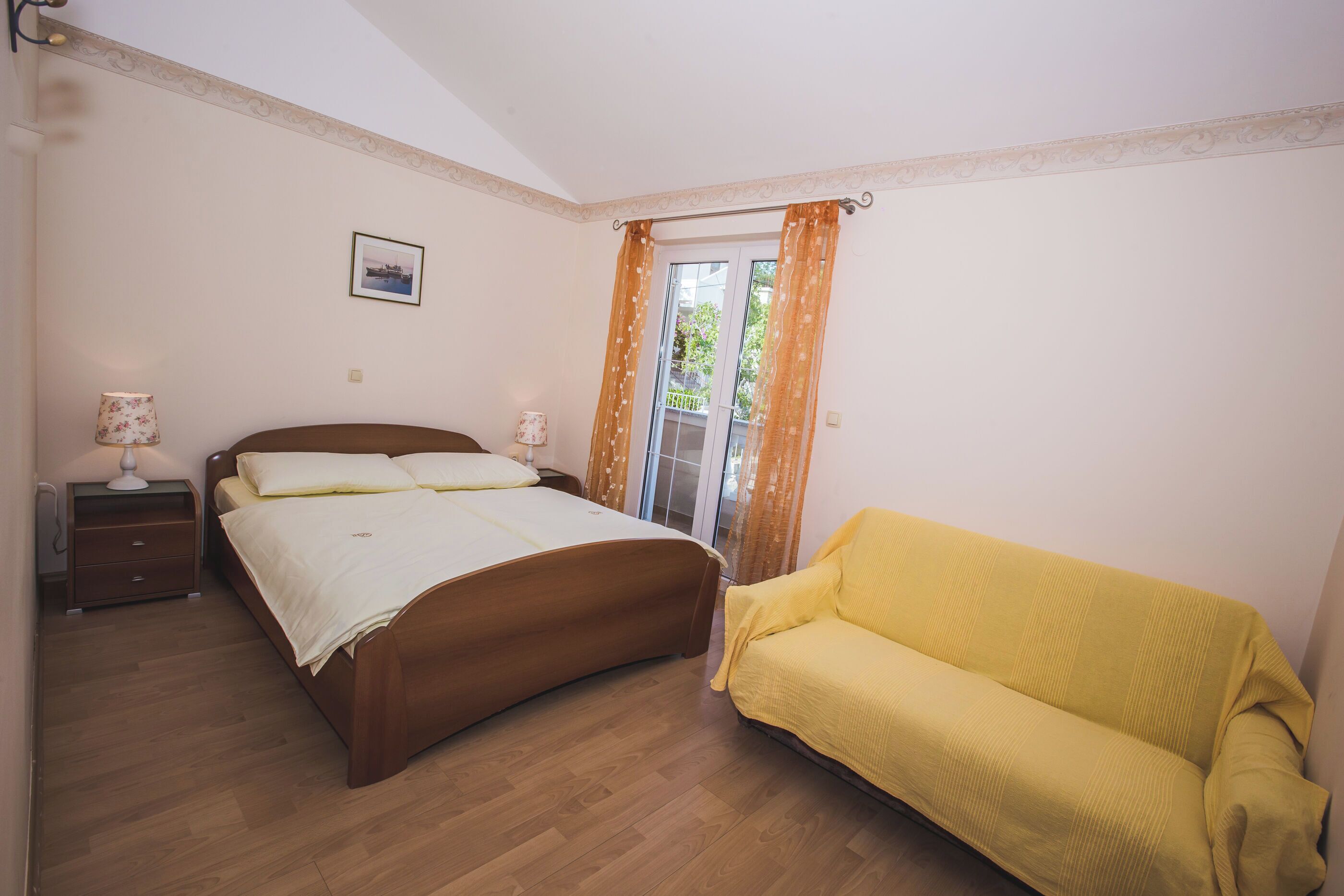 A bedroom with a wooden bed, a yellow sofa, a nightstand, and a window with curtains.
