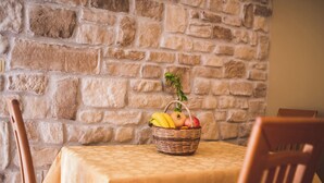A table with a woven basket containing fruits and a small plant, set against a stone wall. - Apartments Anamarija S (Lopar)