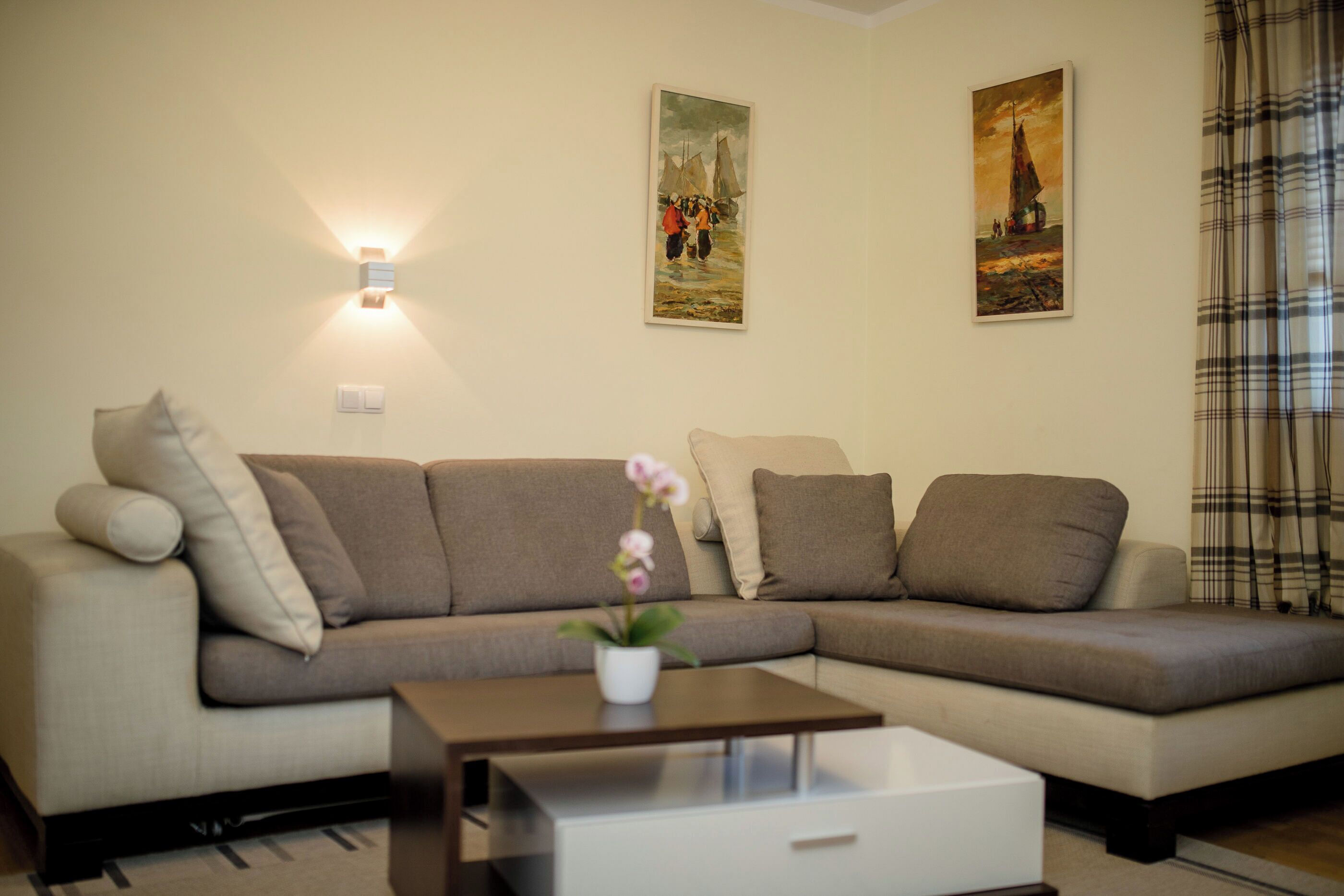 A modern living room with a sectional sofa, a coffee table, and two wall-mounted paintings.