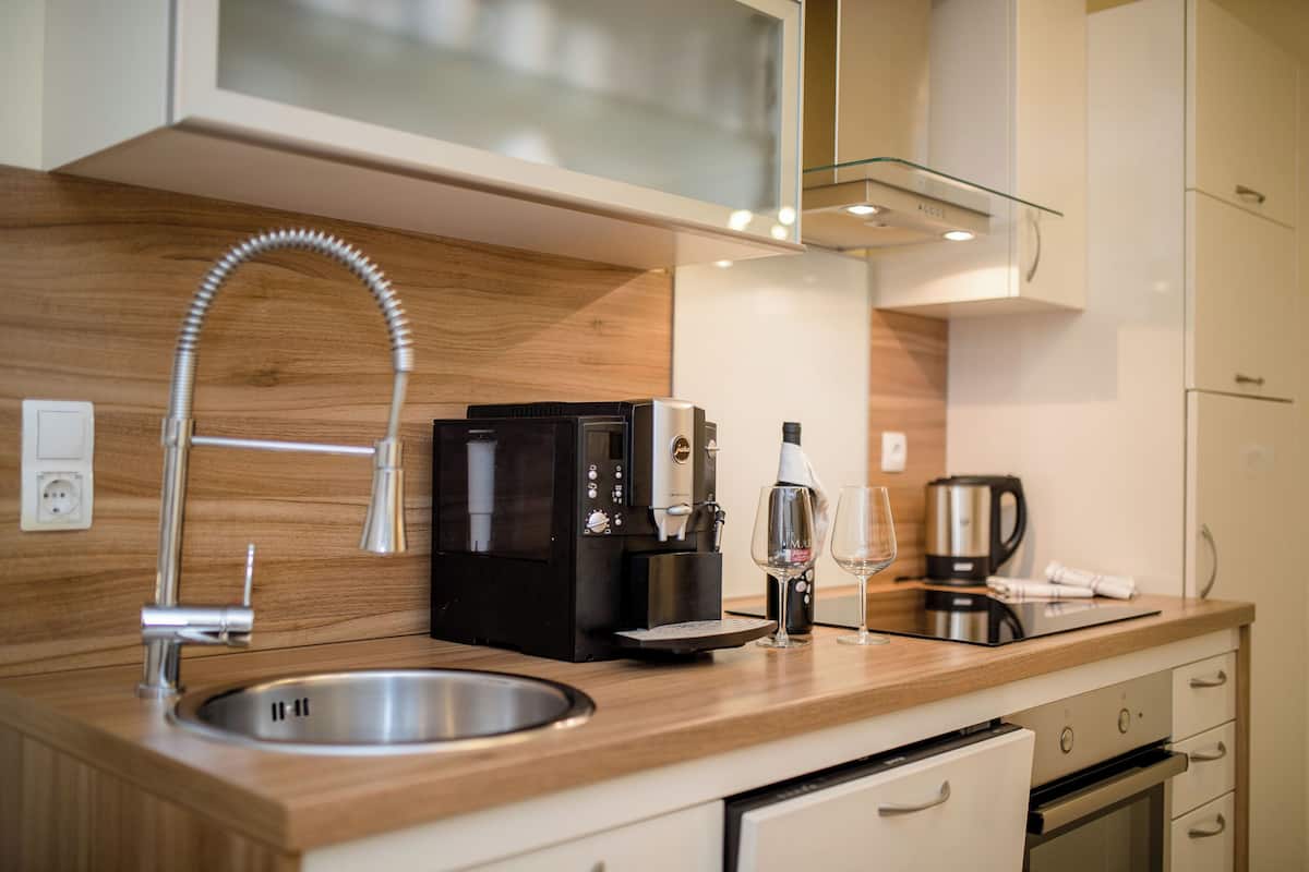 A modern kitchen with a stainless steel sink, a coffee machine, and a wine glass on the counter.