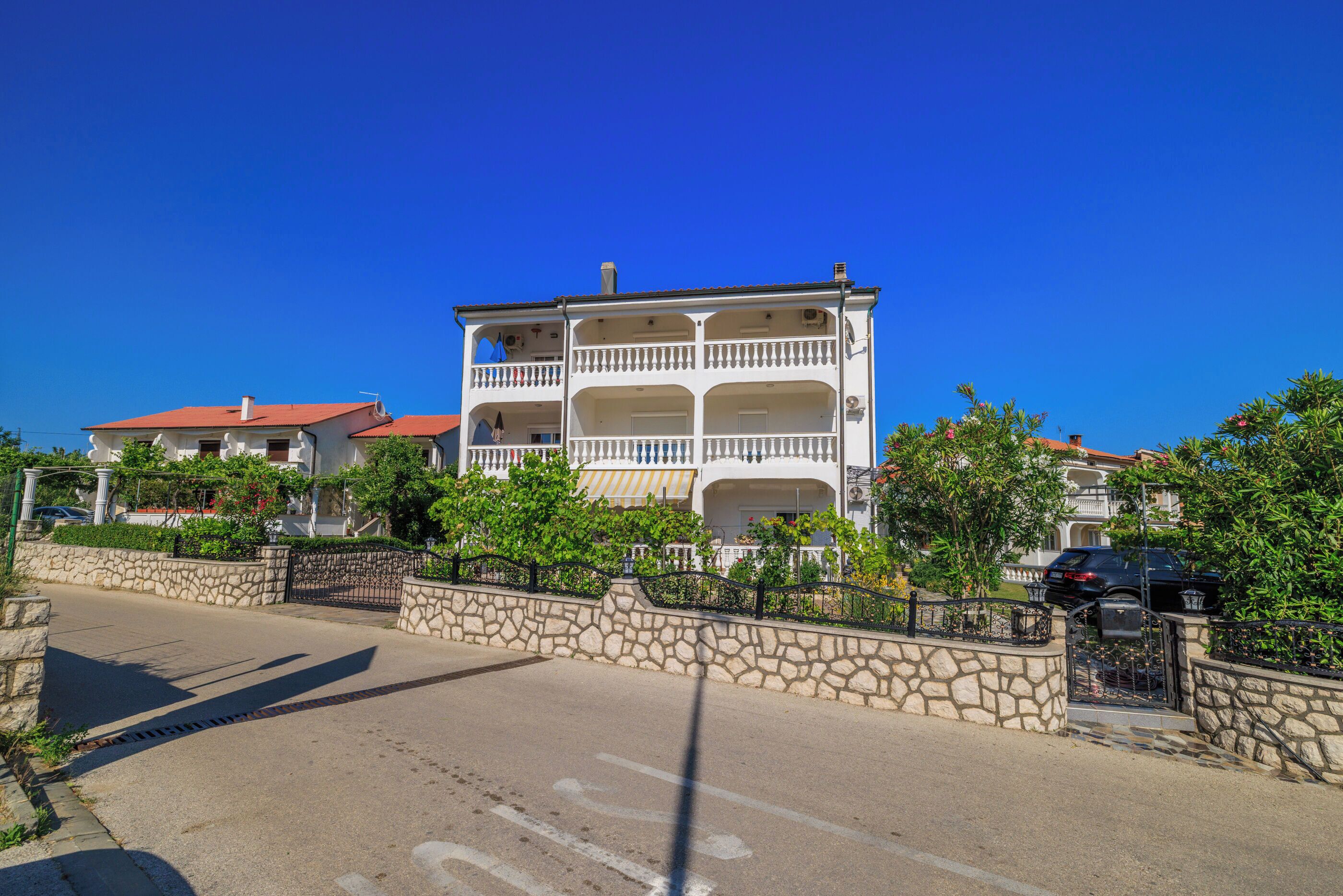 A multi-story building with balconies, a stone wall, and a clear blue sky.