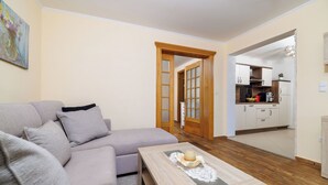Una sala de estar con sofá, una mesa baja con vela, y una cocina visible a través de una puerta abierta.