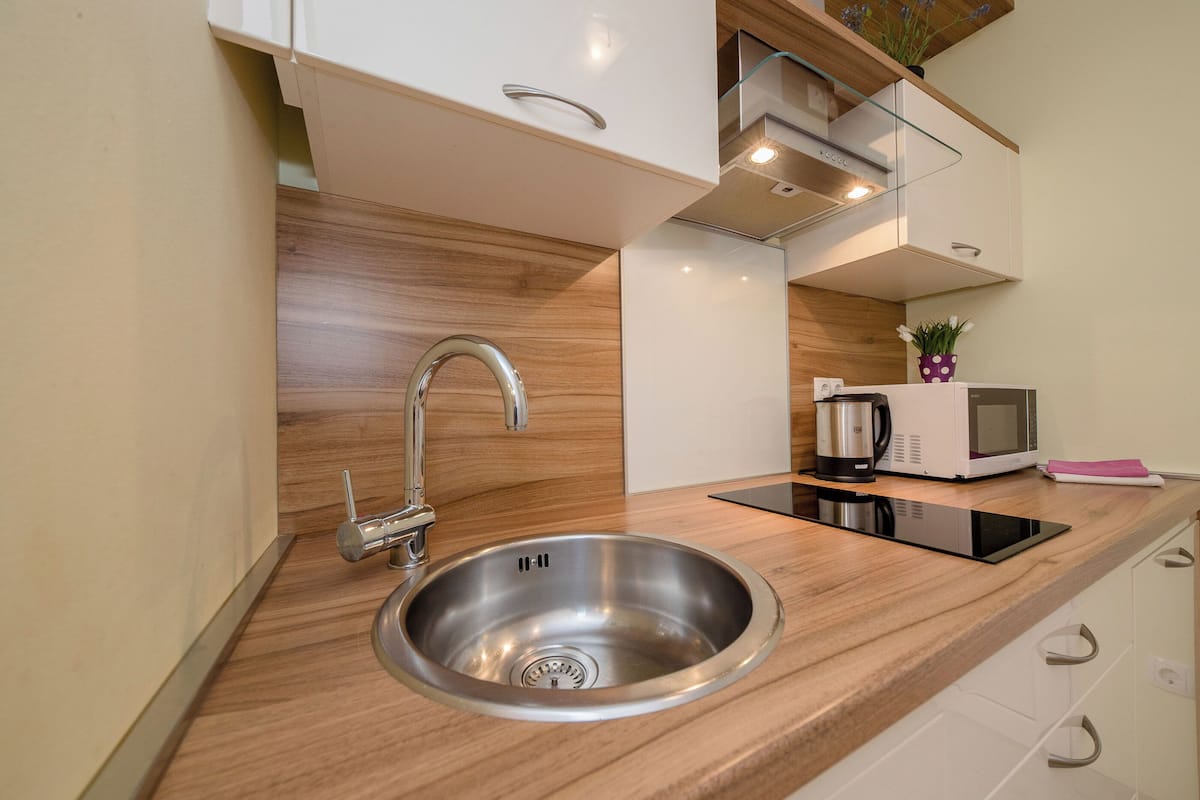 A modern kitchen with a stainless steel sink, wooden countertop, white cabinets, and a microwave.
