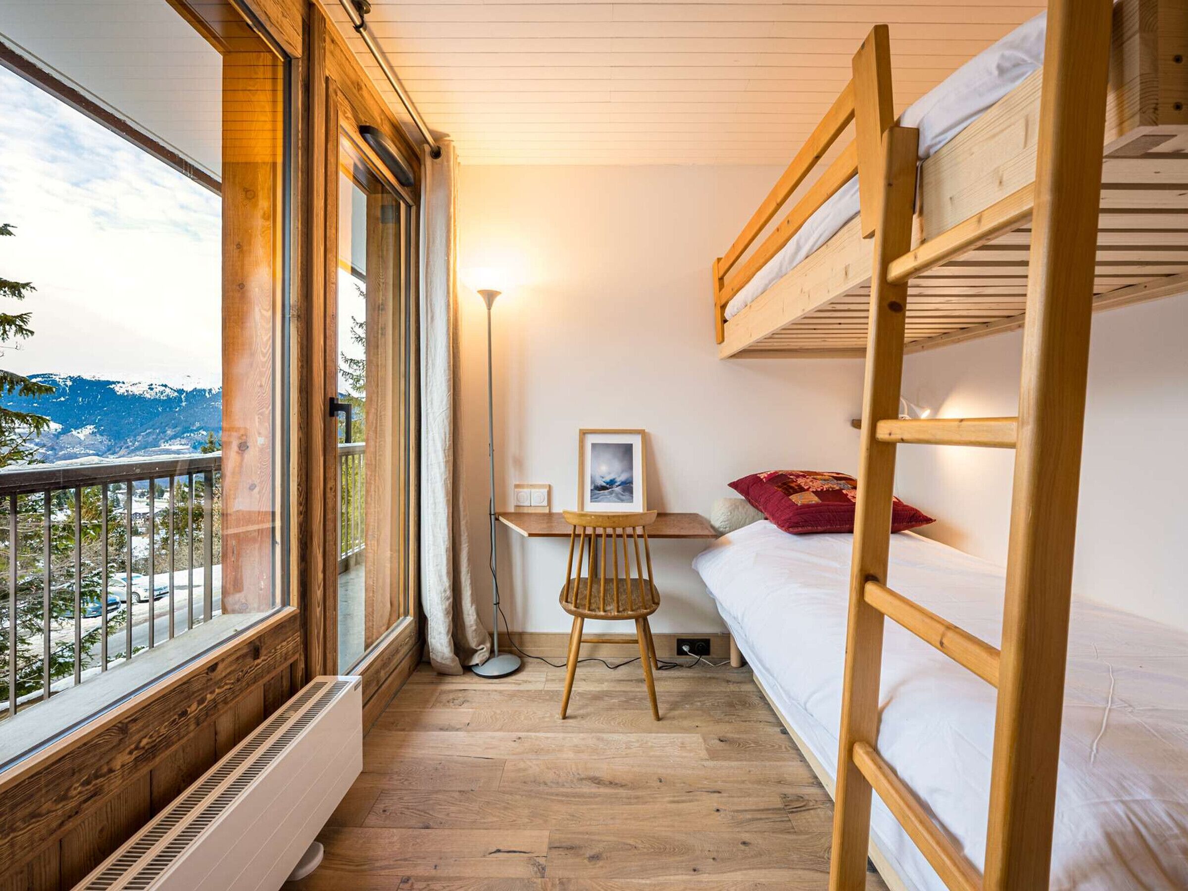 A compact room with a bunk bed, a desk with a chair, and a large window overlooking a snowy mountain.