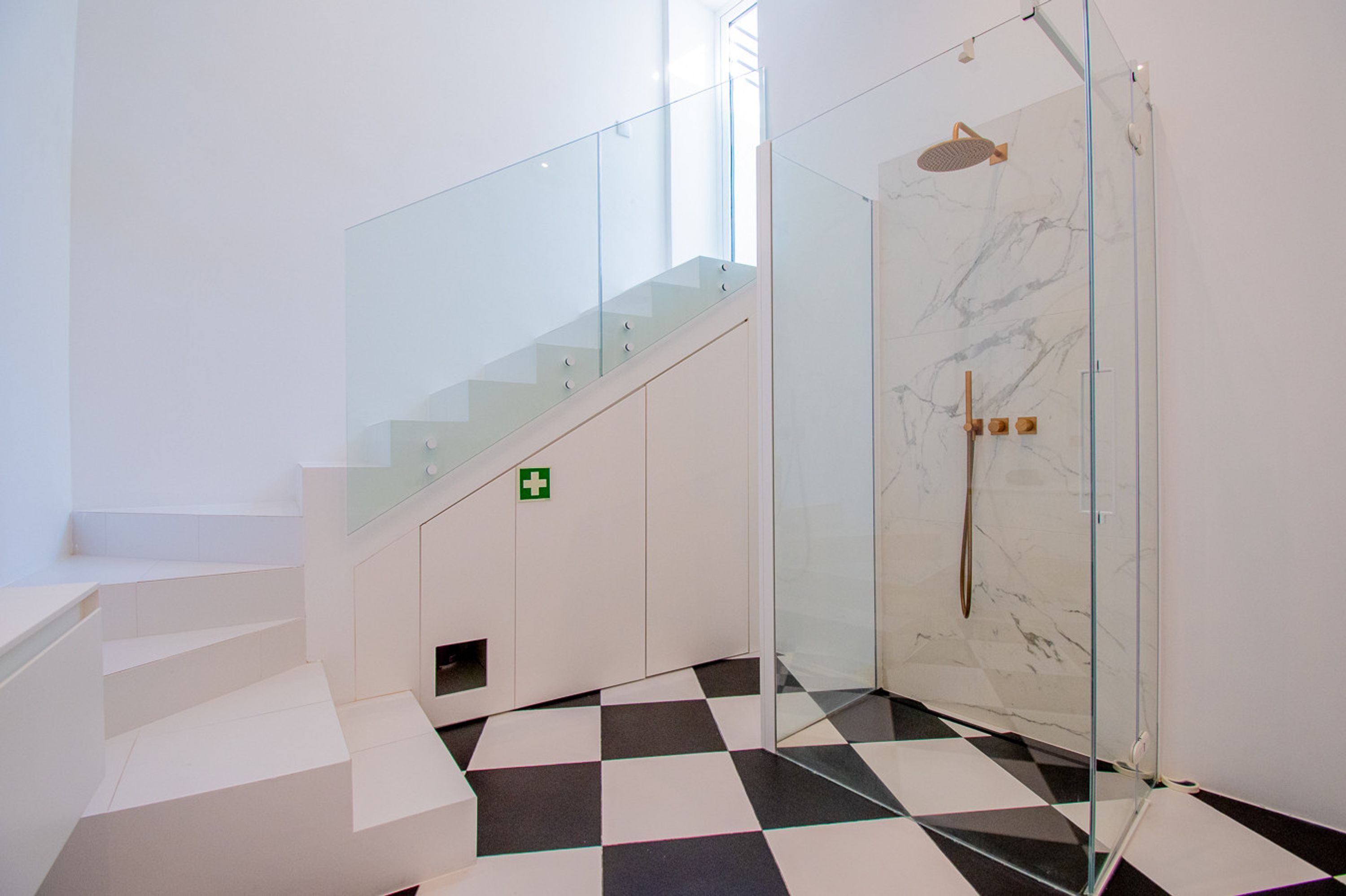 A modern bathroom with a glass shower enclosure, a checkered floor, and a staircase with glass railings.
