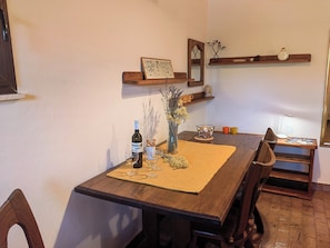 A dining table with a bottle of wine, a vase with dried flowers, and a placemat. There are wooden chairs around the table, and a wooden shelf above it with decorative items. - Apartment Lada (Crikvenica)