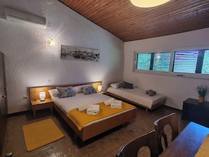A bedroom with a large bed, a smaller bed, a desk, and a window with blinds. - Apartment Lada (Crikvenica)