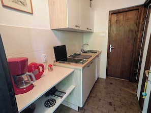 A compact kitchen with white cabinets, a wooden door, a sink, and a red coffee maker. - Apartment Lada (Crikvenica)
