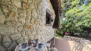 An outdoor patio with a stone wall, a table set with cups and saucers, and metal chairs. - Apartment Lada (Crikvenica)