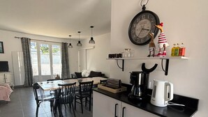 Une cuisine moderne équipée d’une table à manger, de chaises, d’une machine à café, d’une bouilloire et d’une horloge murale.