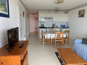 A compact living space with a dining area, kitchen, and a TV on a wooden stand. - Apartment in Fort-Mahon-Plage: near the beach, cozy (Fort-Mahon-Plage)