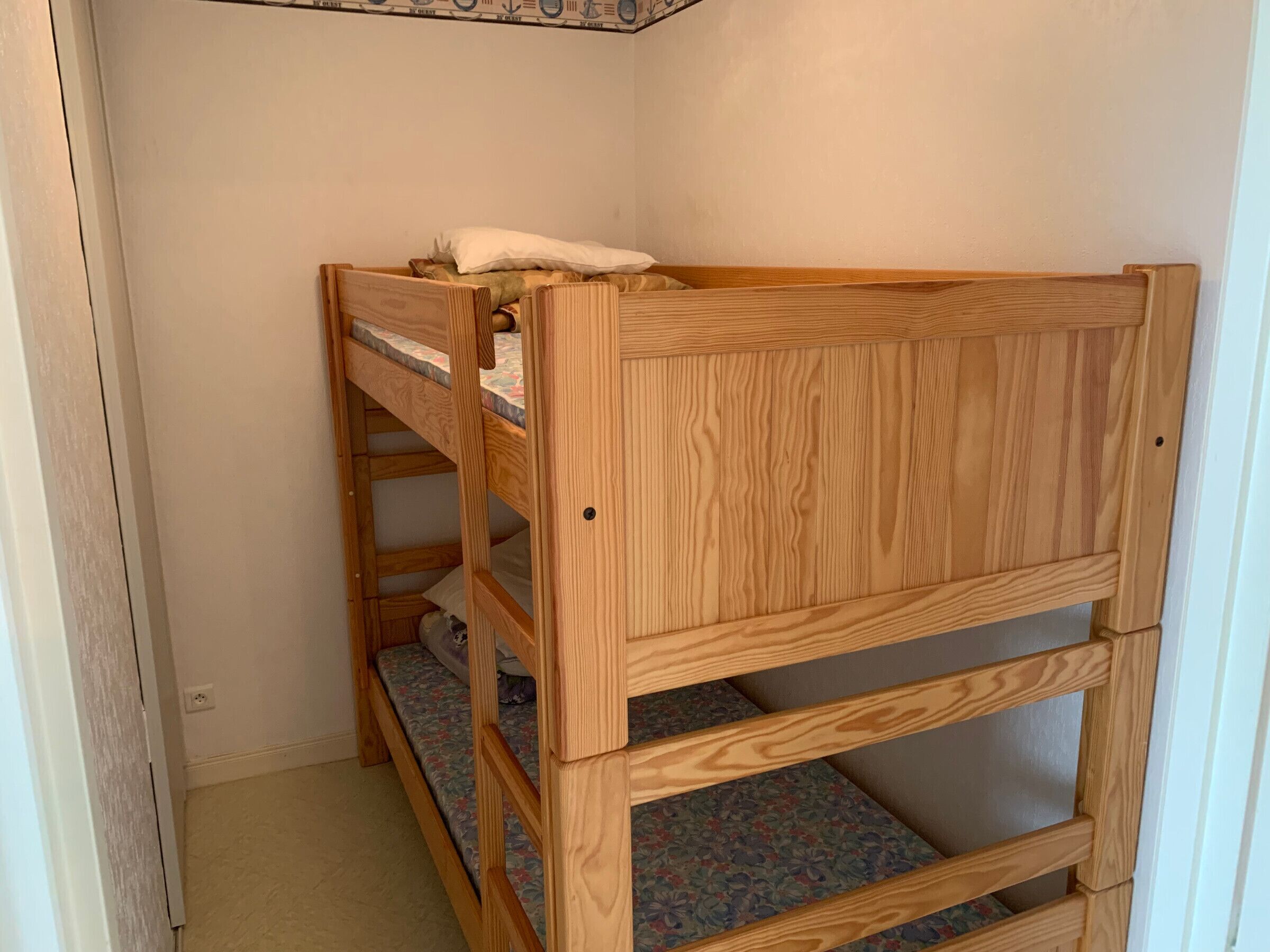 A wooden bunk bed with a floral mattress cover in a room with plain walls and a door on the left.