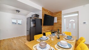 Un comedor moderno con una mesa de madera para cuatro personas, sillas amarillas, un refrigerador negro y un televisor de pantalla plana montado en la pared.