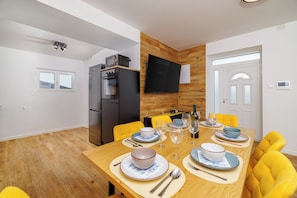 A modern dining area with a wooden table set for four, yellow chairs, a black refrigerator, and a flat-screen TV mounted on the wall. - House Scaena (Crikvenica)